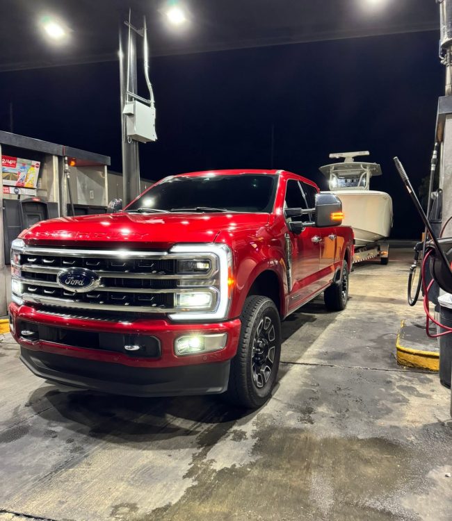 Red Ford Super Duty truck towing a center console boat at a fuel stop at night in Southwest Florida